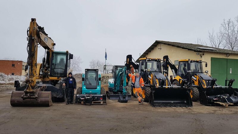 A géppark felsorakoztatva a telephelyen: CAT forgókotró, kompakt rakodó, két lánctalpas minikotró és két JCB kotró-rakodó, mellettük két munkatárs