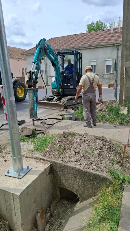 Minikotró hidraulikus törőfejjel bontja a betonburkolatot egy kapubejáró alatti áteresznél